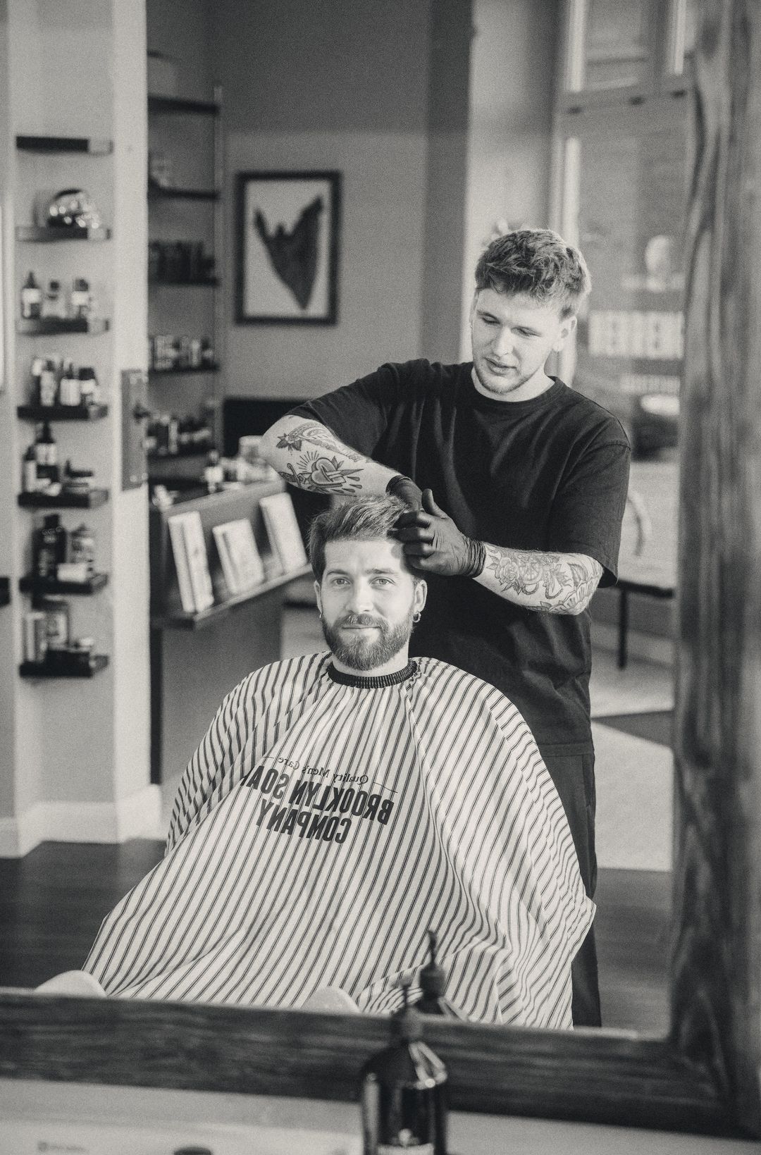 A Herrengut barber cutting a customer’s hair, seen in the mirror (black and white)