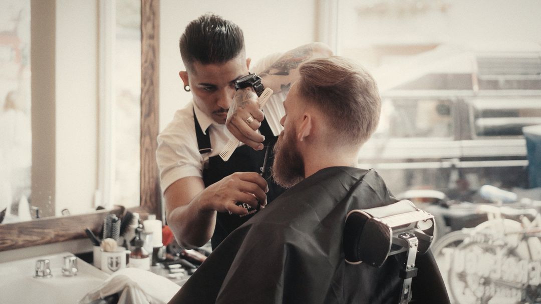 A Herrengut barber trimming a customer’s beard by the window