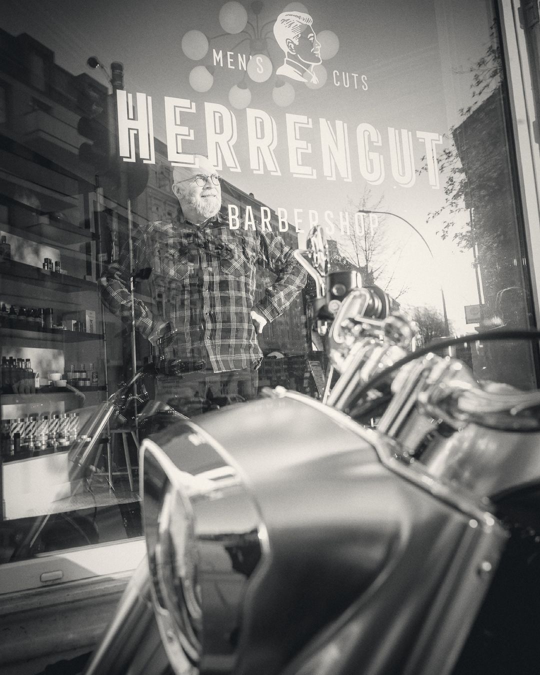 Thorsten Schwermer behind the Herrengut shop window, a motorbike in the foreground (black and white)